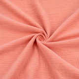 Double gaze de coton corail présentée en gros plan pour révéler sa texture douce et froissée