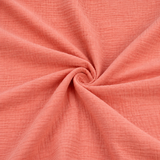 Double gaze de coton corail présentée en gros plan pour révéler sa texture douce et froissée